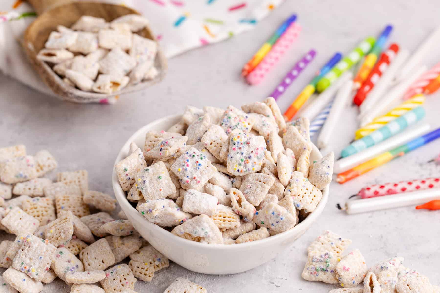 Cake Batter Puppy Chow in a bowl with candles in the back and more cereal in the front