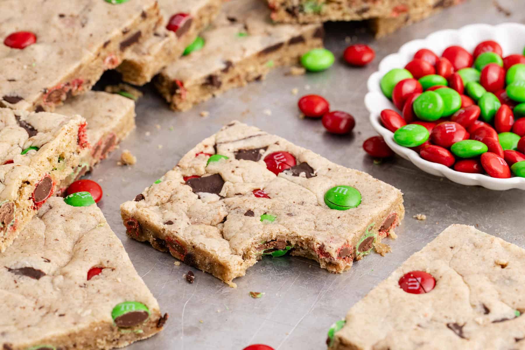 Christmas M&M Cookie Bars on a sheet pan and one has a bite taken