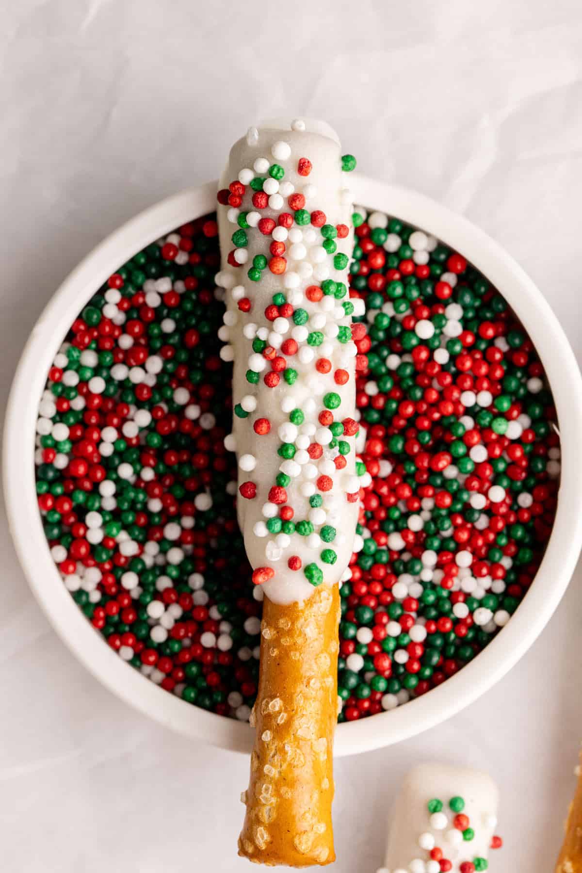 Christmas Pretzel Rods sitting on a bowl of sprinkles from above