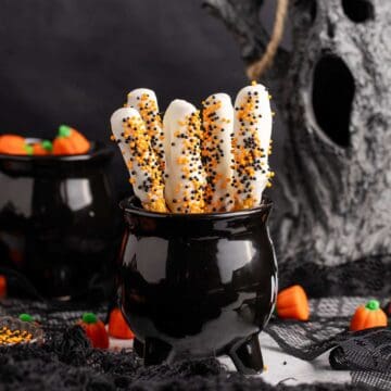 Halloween Pretzel Rods in a cauldron with creepy decor in the back