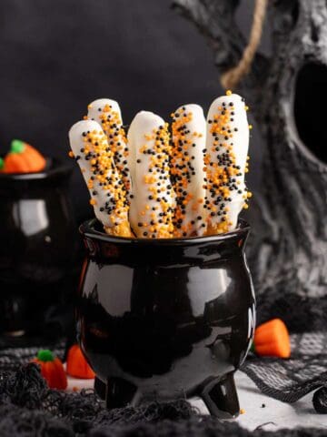 Halloween Pretzel Rods in a cauldron with creepy decor in the back