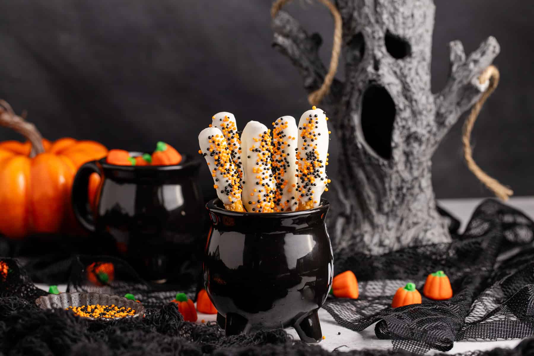 Halloween Pretzel Rods in a cauldron with creepy decor in the back