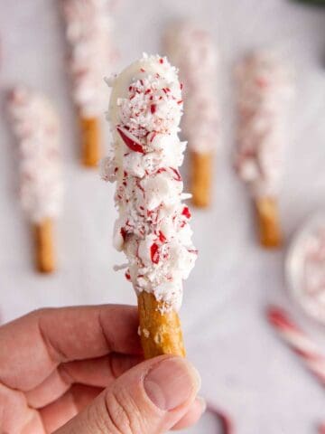 Christmas Pretzel Rods on parchment paper with one being picked up
