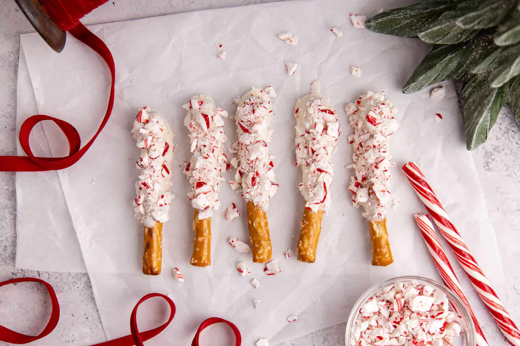 Christmas Pretzel Rods on parchment paper with ribbons and peppermint sticks