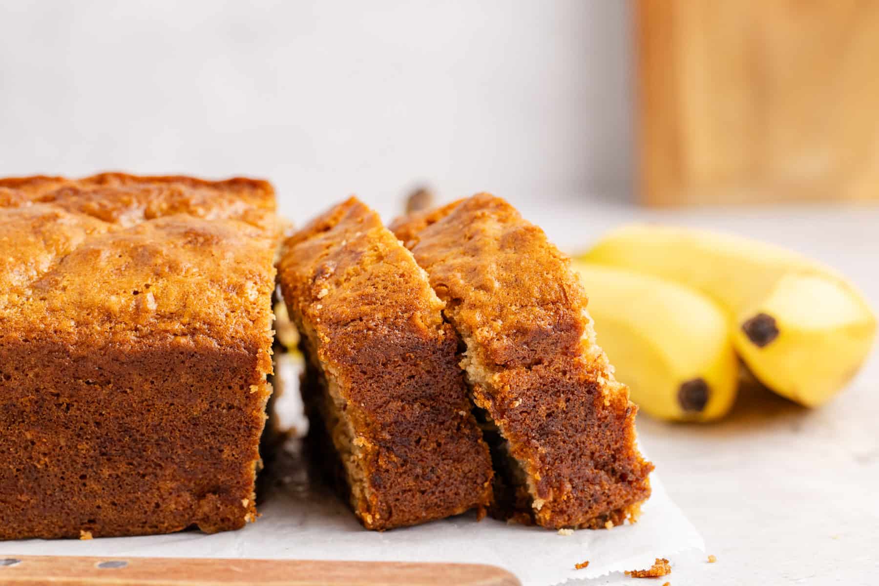 Banana Bread slices cleaning up against the loaf on a cutting board from the side