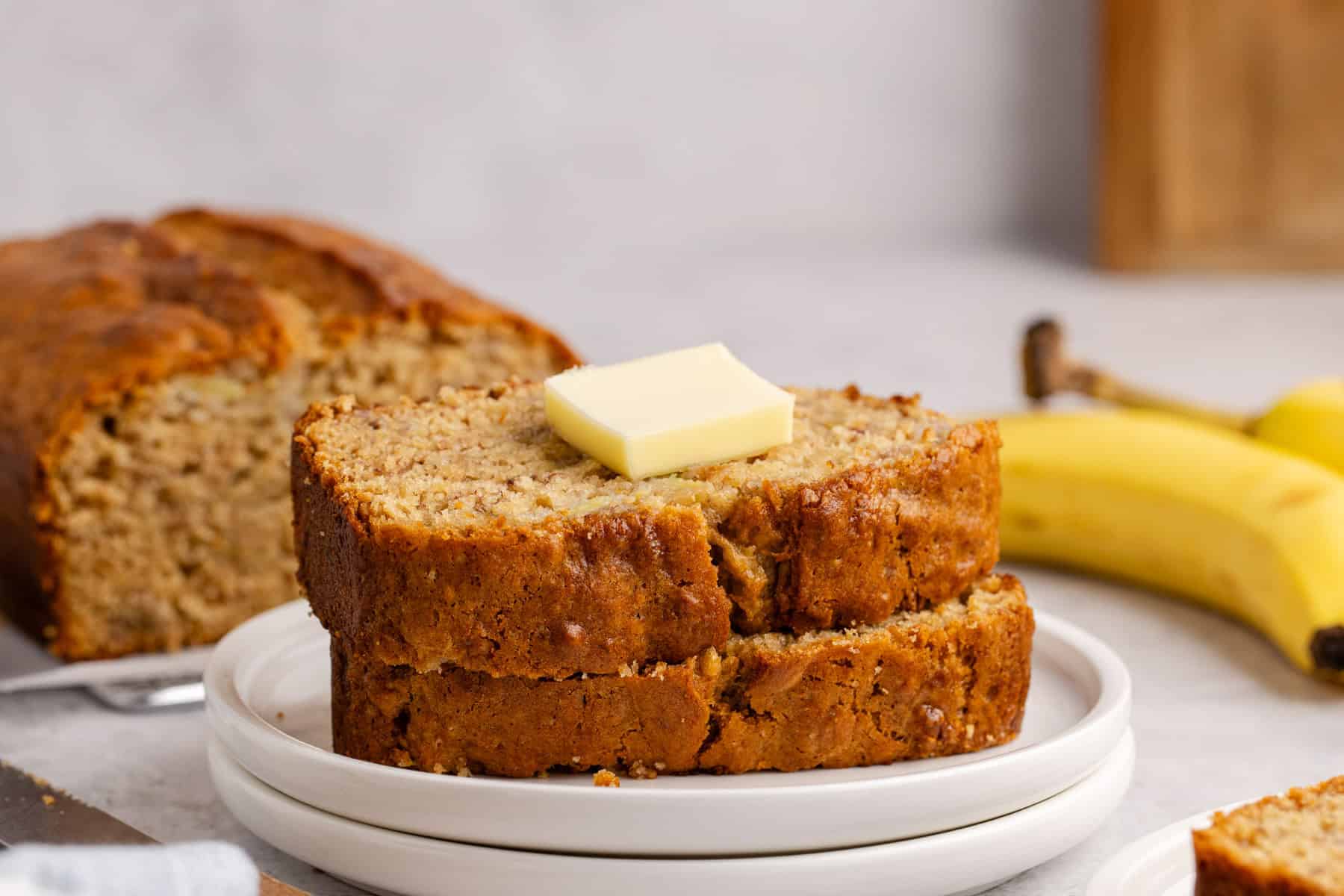 Banana Bread slices stacked on a plate with a pat of butter
