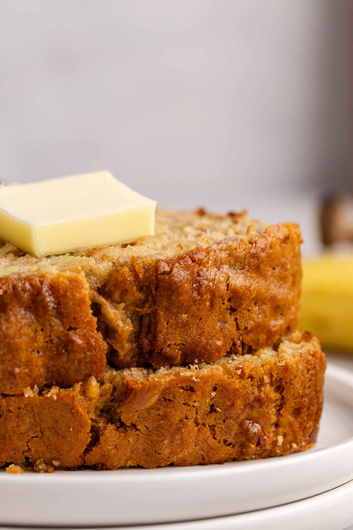 Banana Bread slices stacked on a plate with a pat of butter up close