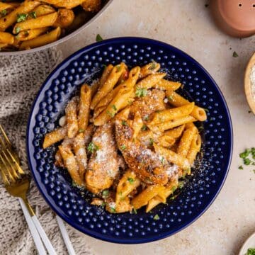 Bang Bang Chicken Pasta served in a blue bowl with a skillet and cheese beside it