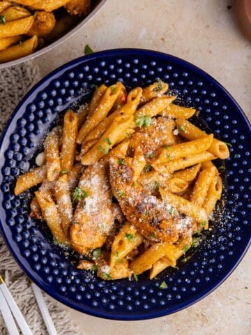 Bang Bang Chicken Pasta served in a blue bowl with a skillet and cheese beside it