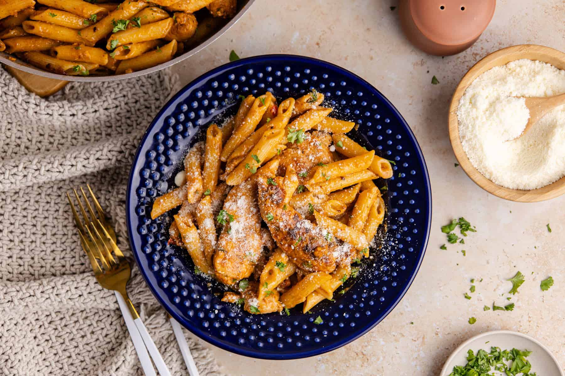 Bang Bang Chicken Pasta served in a blue bowl with a skillet and cheese beside it