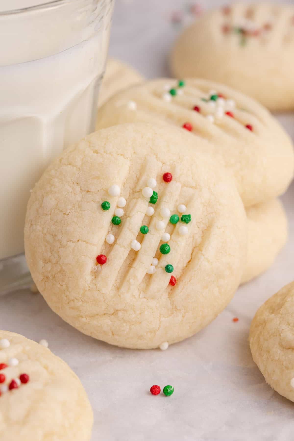 Whipped Shortbread Cookies stacked beside and leaning on a glass of milk