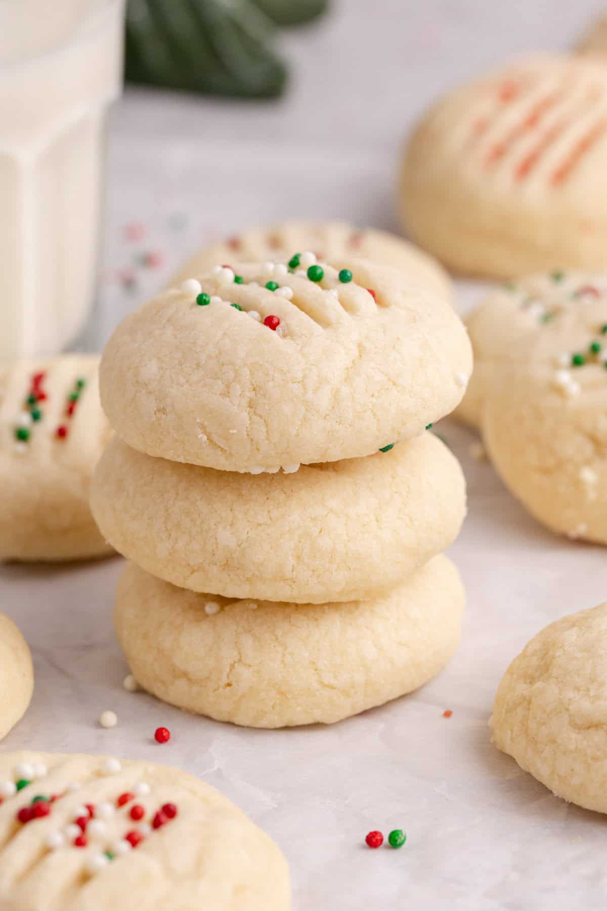 Whipped Shortbread Cookies stacked with a glass of milk in behind